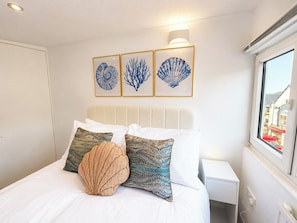 A neatly made bed with white bedding and decorative pillows, a headboard with a light fixture, and framed artwork on the wall.