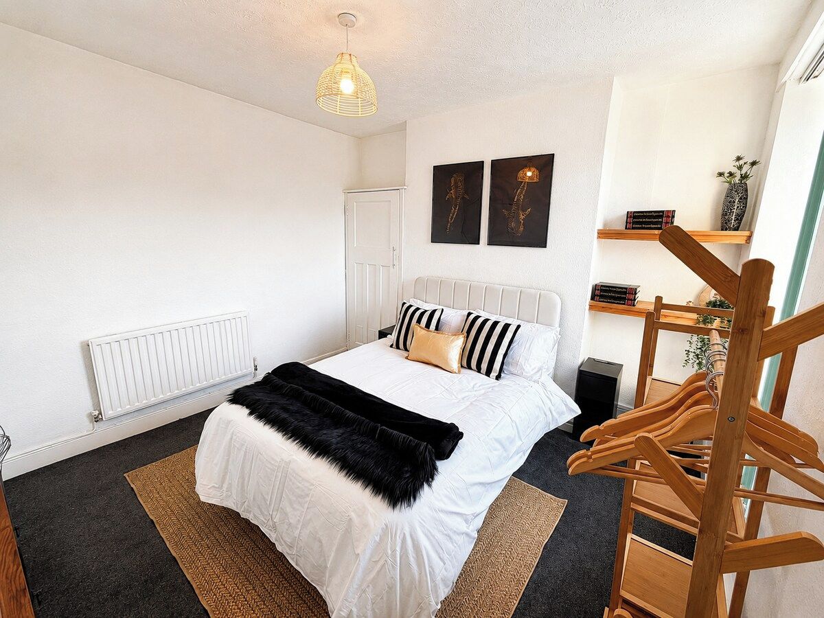 Een slaapkamer met een bed, een radiator, een hanglamp en een houten stoel.