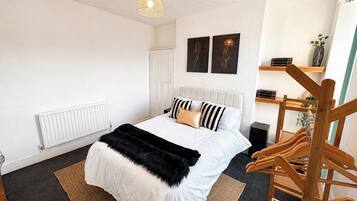 Een slaapkamer met een bed, een radiator, een hanglamp en een houten stoel.