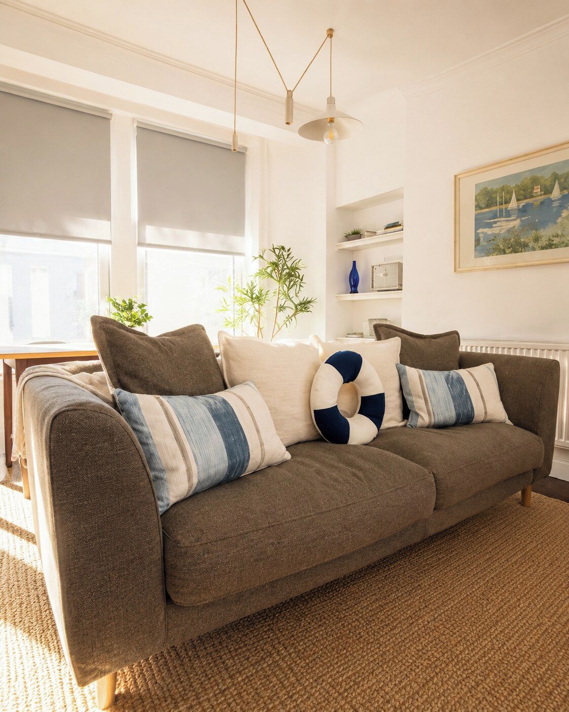 A brown sofa with striped and solid pillows, a woven rug, and a hanging pendant light.