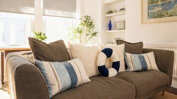 A brown sofa with striped and solid pillows, a woven rug, and a hanging pendant light.