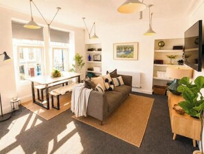 Una sala de estar moderna con un sofá, una mesa de comedor y una mesa de centro. Hay un ventanal que proporciona luz natural y vistas al exterior.