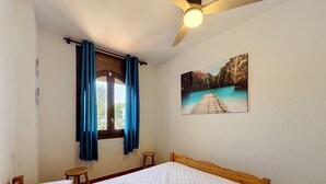 Ein Schlafzimmer mit einem Bett, einem Vorhangfenster, einem Deckenventilator und einem Wandbild.