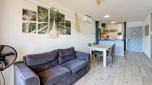 Ein Wohnzimmer mit einer Couch, einem Esstisch und einer Küche im Hintergrund.