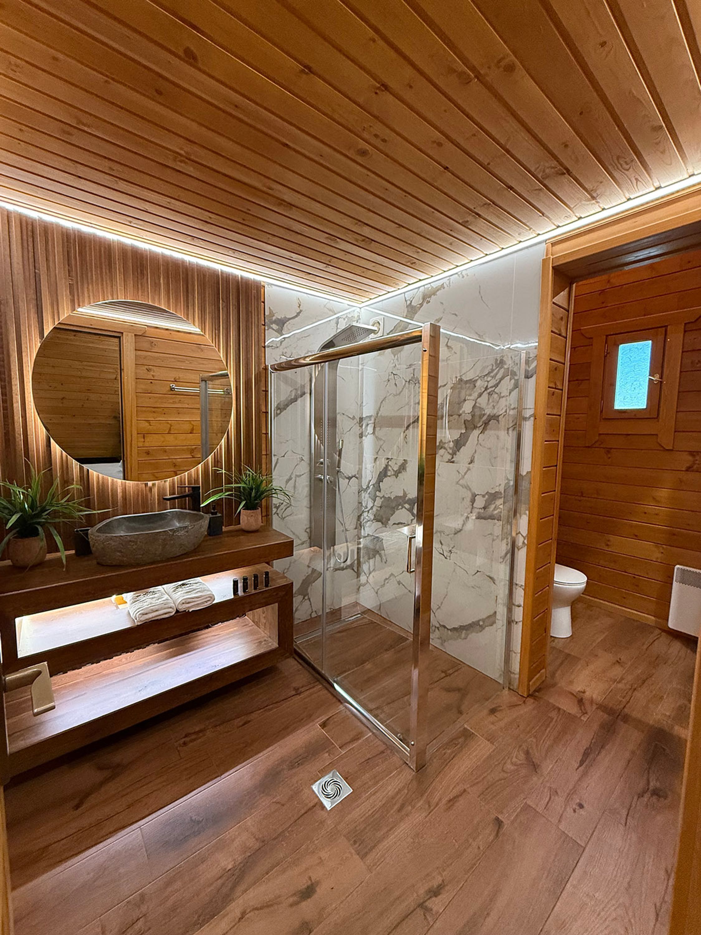 A modern bathroom with a wooden vanity, a glass shower enclosure, and a marble wall.