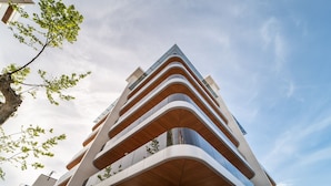 Un bâtiment moderne à plusieurs étages, doté d’une architecture originale aux lignes courbes et agrémenté de balcons avec des garde-corps en bois.