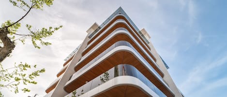 A modern multi-story building with a unique curved architectural design, featuring balconies with wooden railings.