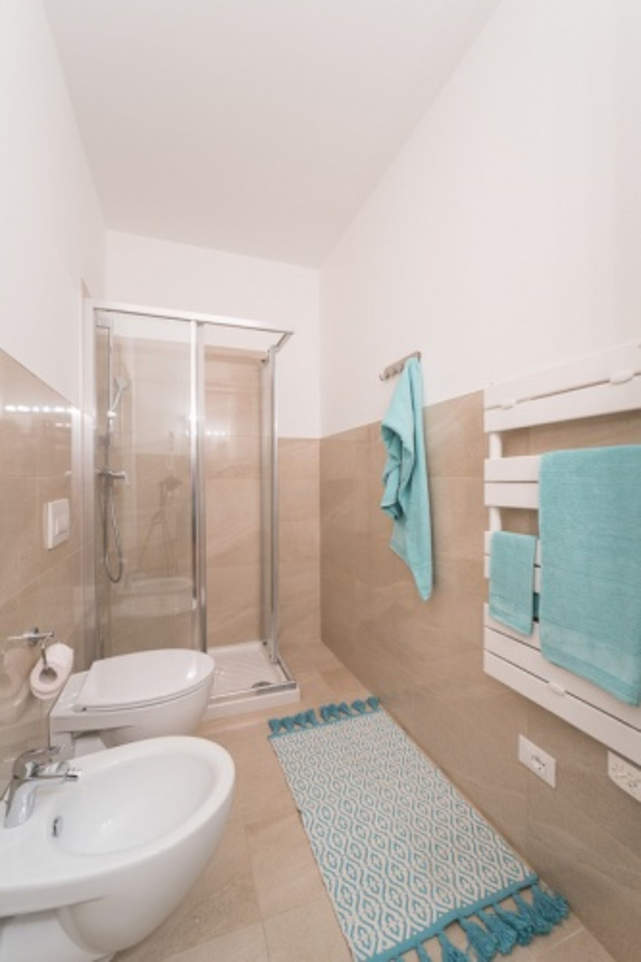 A bathroom with a shower, toilet, sink, and a patterned rug.