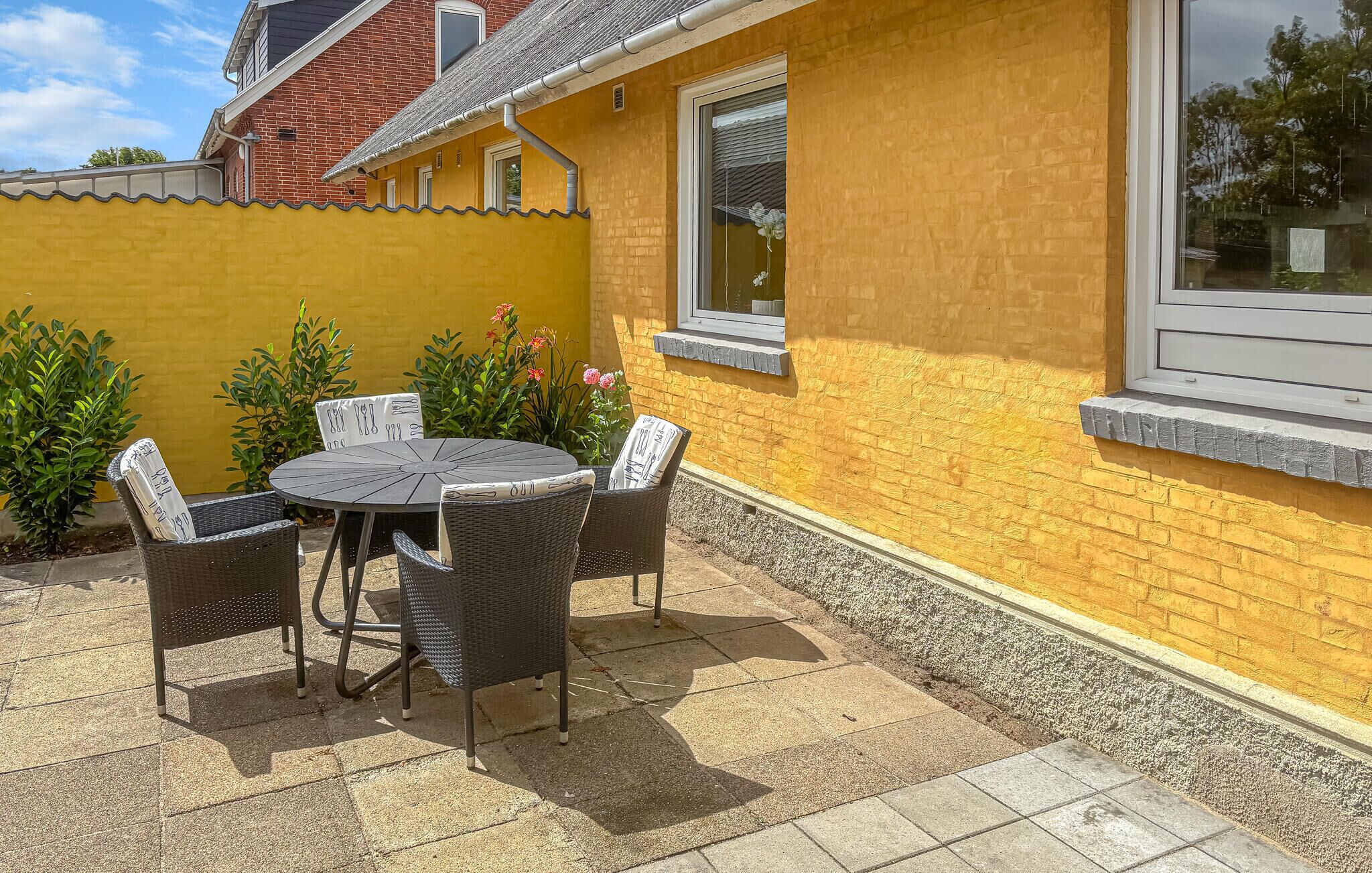 A patio with a round table and four chairs, a yellow brick wall, and a window.