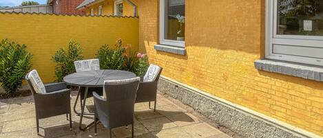 A patio with a round table and four chairs, a yellow brick wall, and a window.