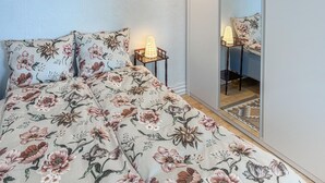 Una camera da letto con una copriletto floreale, un comodino con una lampada e uno specchio a figura intera.
