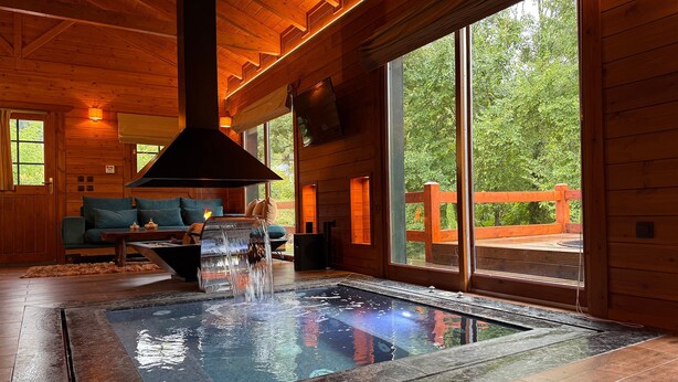A log cabin interior with a stone hot tub, wooden furniture, and large windows offering a view of the outdoors. - Chalet for two (Delphi)