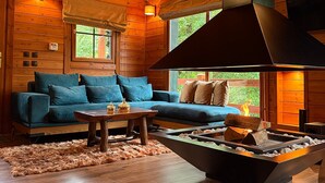 A log cabin interior with a sofa, fireplace, wooden floors, and a ceiling with exposed beams. - Chalet for two (Delphi)
