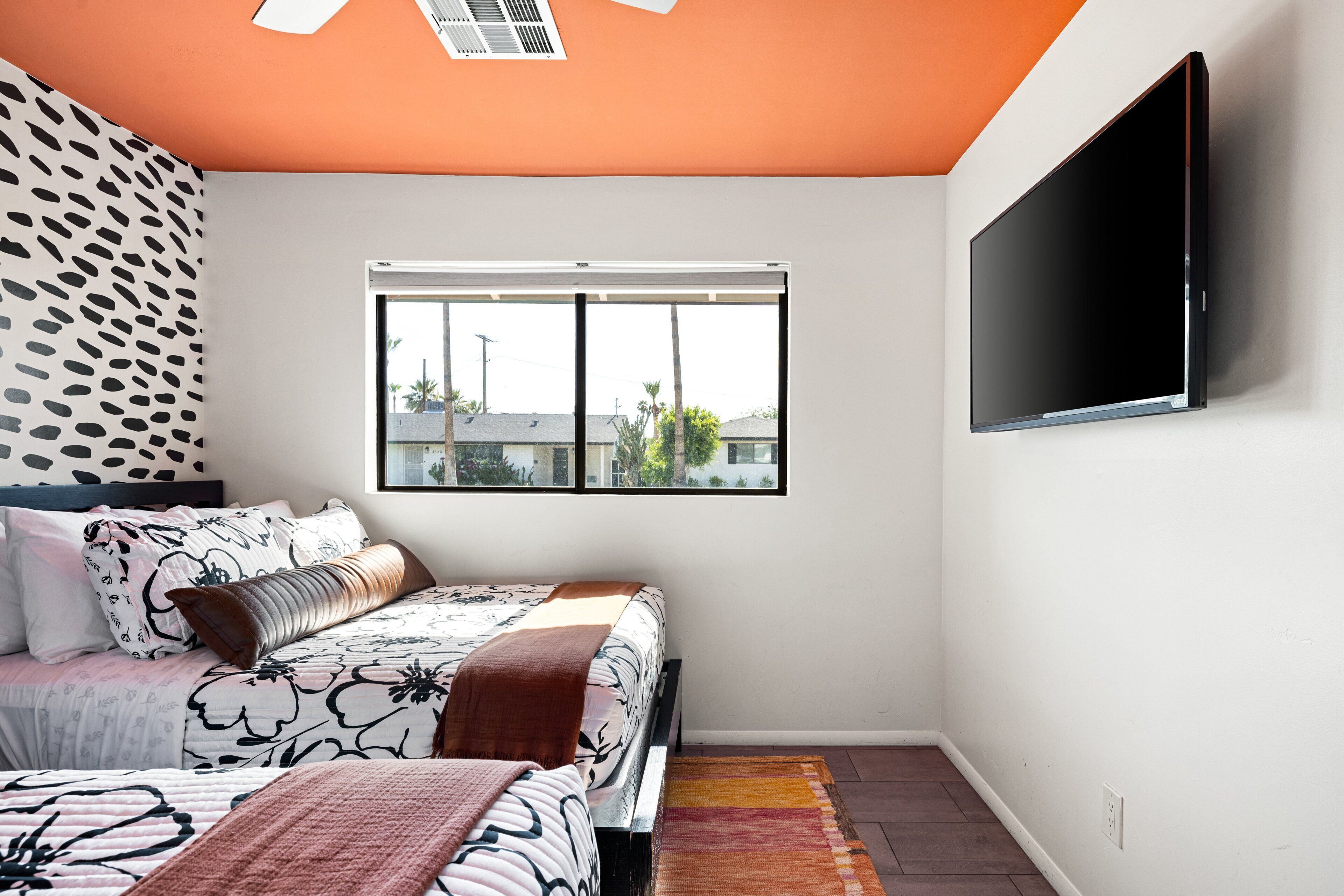 A bedroom with a bed, a window, a wall-mounted TV, and a patterned wall.