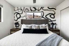 Ein Schlafzimmer mit einem großen Bett, einem Fenster und einer Wand mit abstrakten Schwarz-Weiß-Mustern.
