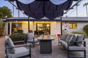 An outdoor patio with a covered seating area, a fire feature, and a view of the house's interior. - Retro-chic home in Old Town Scottsdale! (Scottsdale)