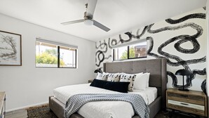 Ein modernes Schlafzimmer mit einem Bett, Nachttischen, einem Deckenventilator und Kunstwerken an den Wänden.
