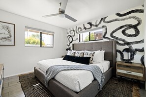 A modern bedroom with a bed, bedside tables, a ceiling fan, and artwork on the walls. - Retro-chic home in Old Town Scottsdale! (Scottsdale)