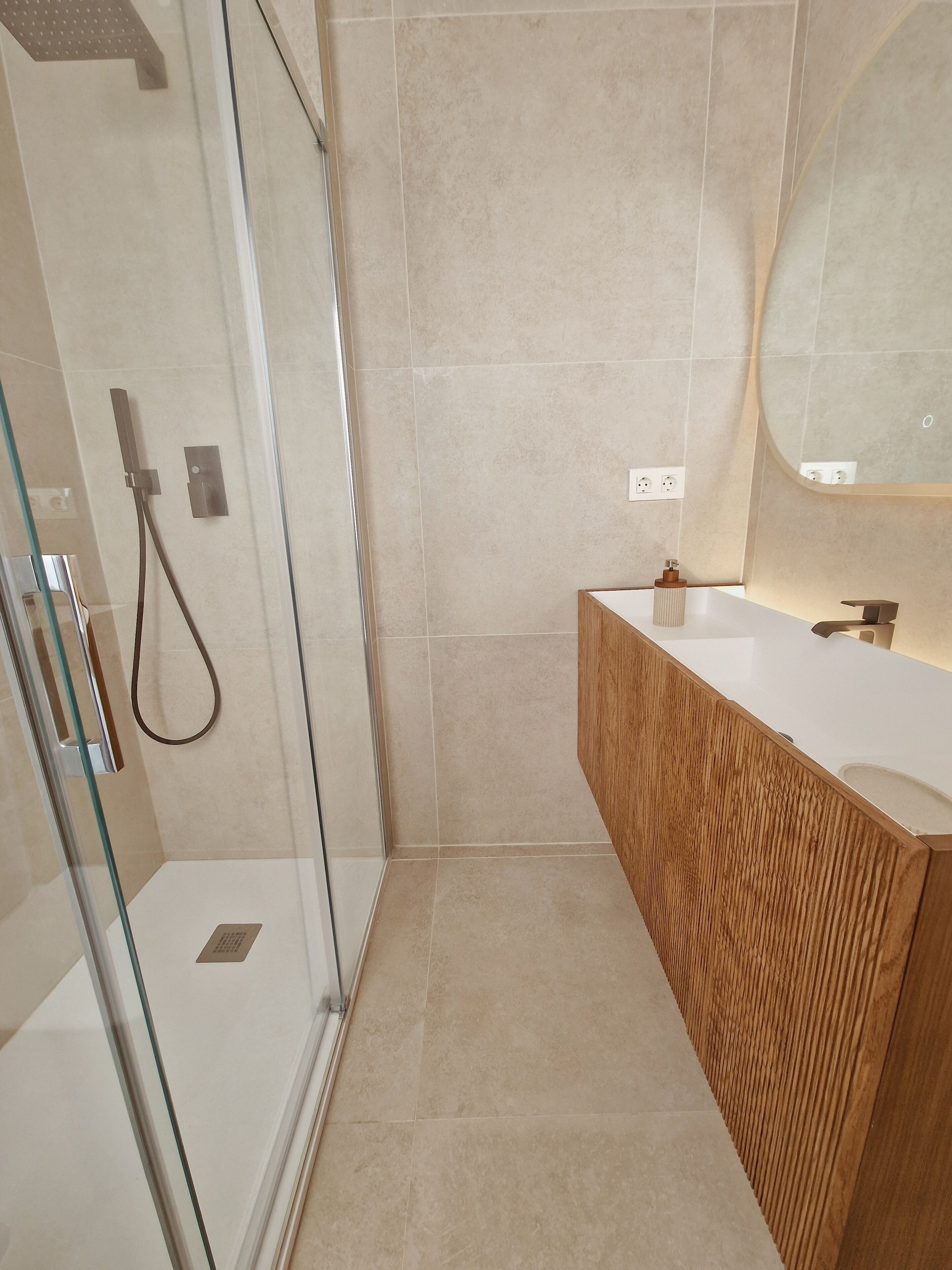 A modern bathroom with a glass shower enclosure, a wooden vanity, and a large mirror.