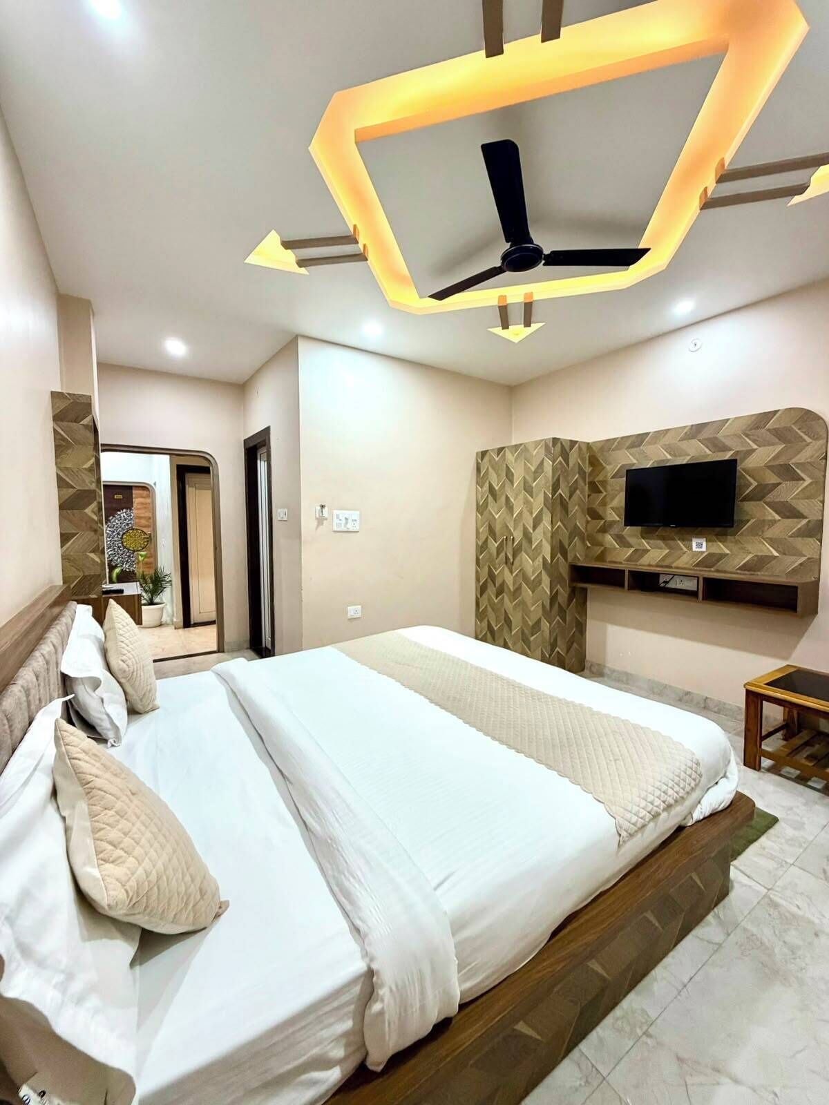 A modern bedroom with a large bed, a flat-screen TV mounted on the wall, and a ceiling fan.
