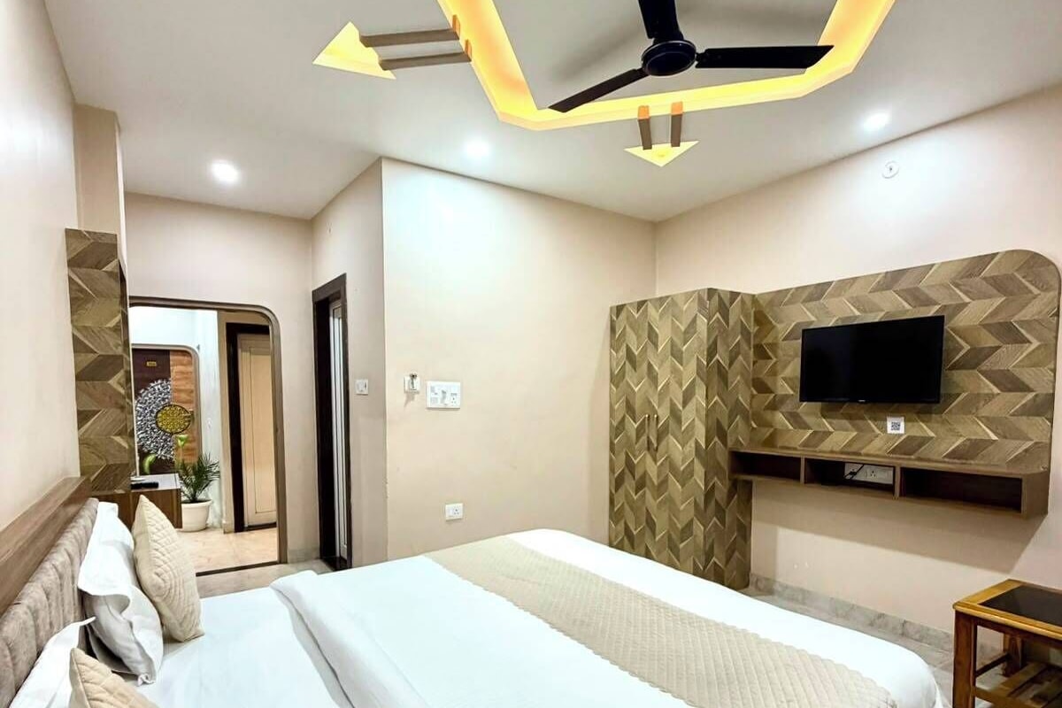 A modern bedroom with a large bed, a flat-screen TV mounted on the wall, and a ceiling fan.