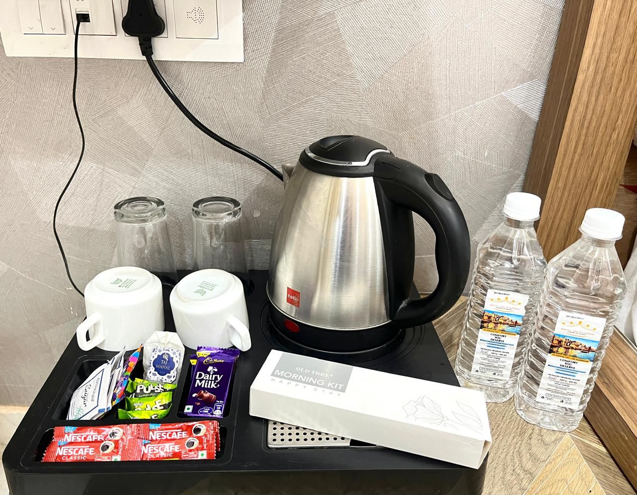 Ett brickbord med frukost, inklusive en kaffebryggare, koppar, mjölk, choklad och vattenflaskor.