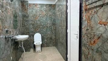 A bathroom with a marble floor, a toilet, a sink, and a shower area.