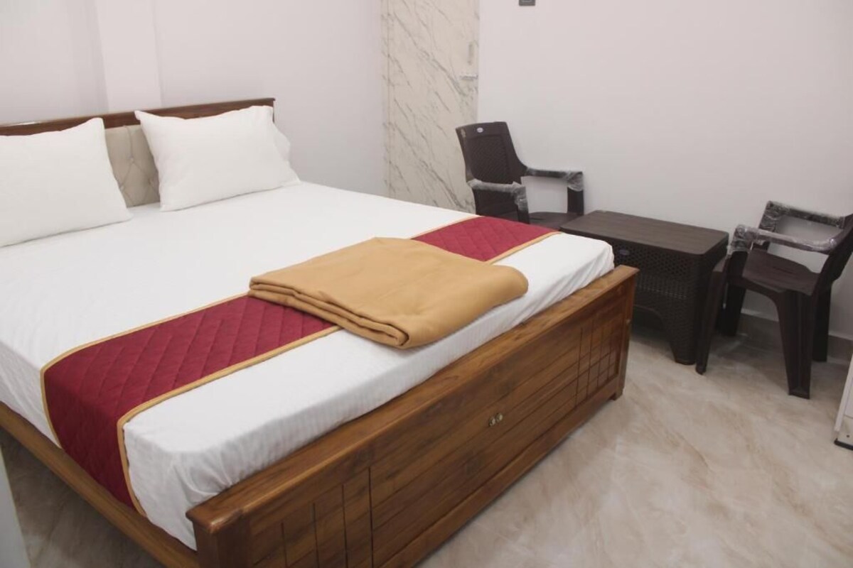 Una habitación de hotel con una cama de madera, ropa de cama blanca, una colcha rojo y dorado, una mesita de noche de madera y una pared de mármol.