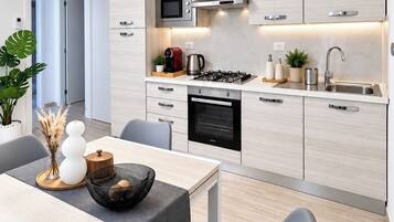 A modern kitchen with a gas stove, microwave, and built-in oven. There is a dining area with a table and chairs, and a decorative plant on the counter.