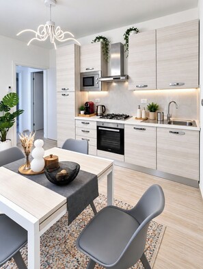 Une cuisine moderne équipée d’une cuisinière à gaz, d’un four à micro-ondes et d’un four encastré. On y trouve un coin repas avec une table et des chaises, ainsi qu’une plante décorative posée sur le plan de travail.