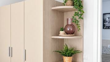 A room with a large wardrobe, a built-in shelf unit with plants, and a framed picture on the wall.