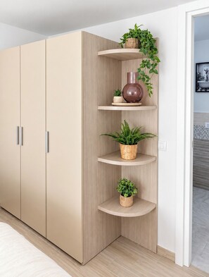 Une pièce dotée d’une grande armoire, d’une bibliothèque intégrée agrémentée de plantes et d’un tableau encadré accroché au mur.