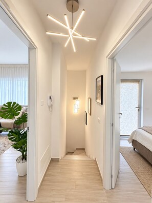 En modern hall med en taklampa, en krukväxt och en säng som syns i bakgrunden.