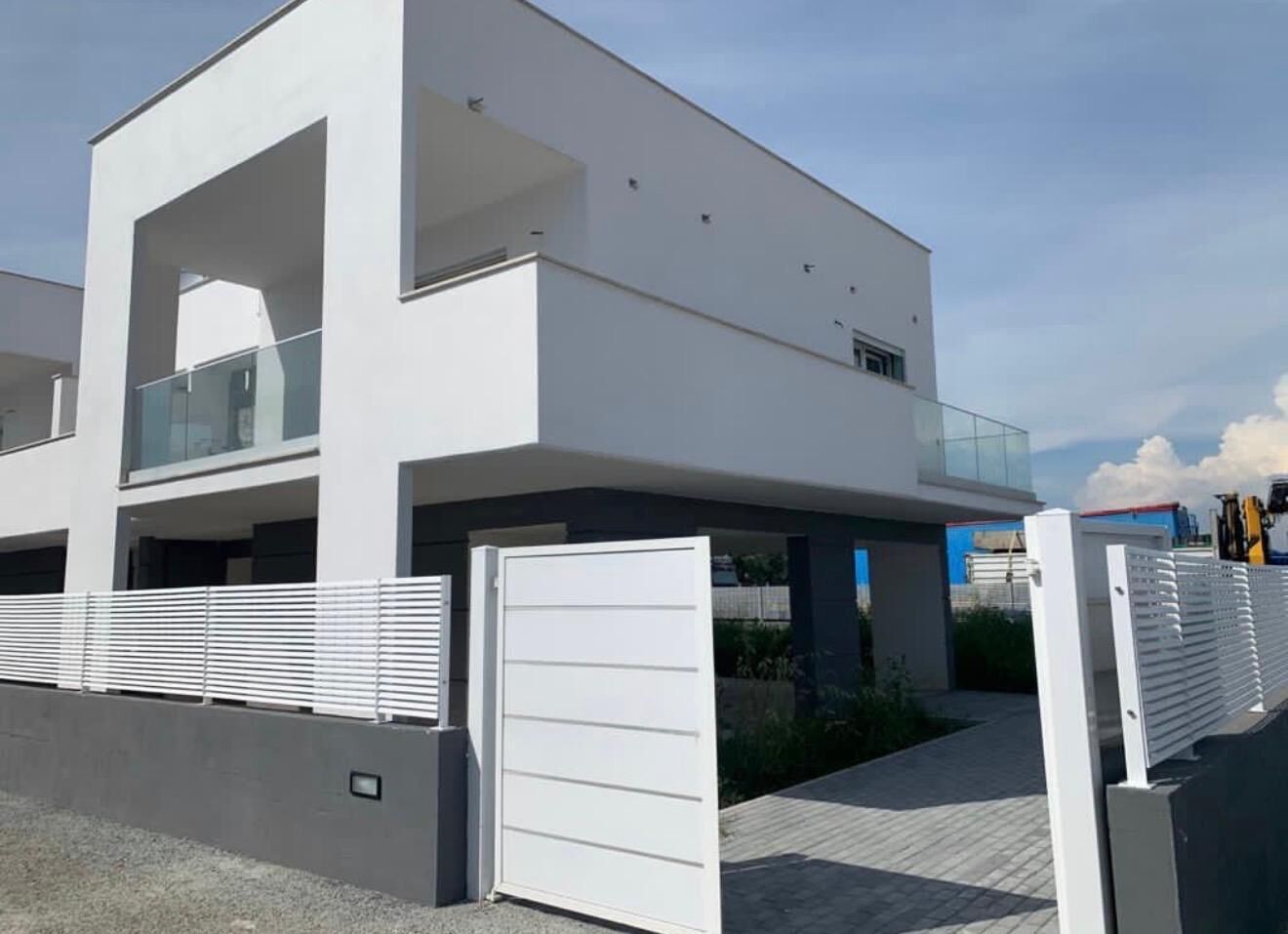 A modern two-story building with a flat roof, large windows, and a gated entrance.