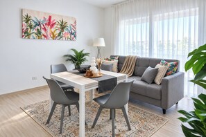 Un salon moderne avec une table à manger, un canapé gris et une grande fenêtre ornée de rideaux légers.