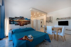 A modern hotel room with a large bed, a dining area, and a TV. - GuestHost - Oasi Azzurra Apartment (Bari)