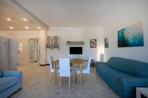 Een moderne woonkamer met een eethoek, een bank en een aan de muur bevestigde televisie.