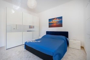 Ein Schlafzimmer mit einem Bett, einem Nachttisch, einem Kleiderschrank und einem Sonnenuntergangsbild.