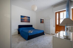 Een slaapkamer met een bed, een bureau, een lamp en twee schilderijen aan de muur.