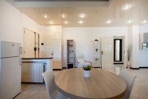 A modern kitchen with white cabinets, a built-in oven, and a round wooden dining table with chairs. - GuestHost - Oasi Azzurra Apartment (Bari)
