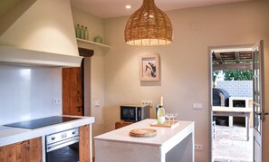 A kitchen with a microwave, a wooden cabinet, a hanging light fixture, and a small table with a bottle and glasses. - Peace and elegance in a Catalan country house with a pool, 3 km from the beach. (Torroella de Montgrí)
