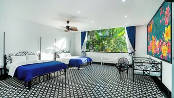 Une chambre d’hôtel avec deux lits, un ventilateur de plafond, une grande fenêtre avec des rideaux, un radiateur et un tableau accroché au mur.