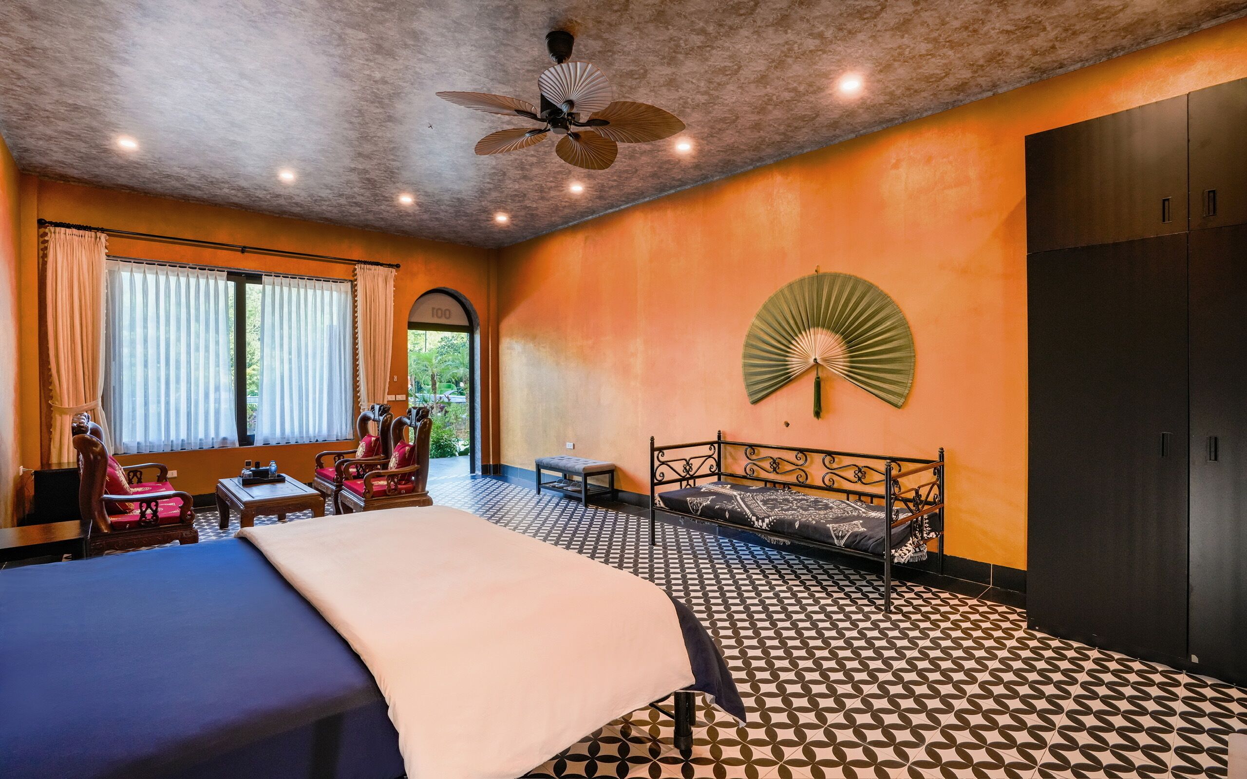 Une chambre d’hôtel équipée d’un lit, d’un bureau, d’une chaise, d’un ventilateur et d’une armoire.