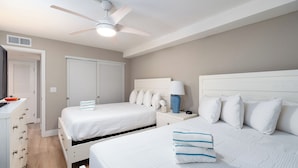 Une chambre d’hôtel avec deux lits, un ventilateur de plafond, une table de chevet avec une lampe et une salle de bain avec douche.