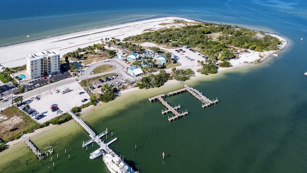 Vue aérienne d’une station balnéaire comprenant un port de plaisance, plusieurs bâtiments et une plage.