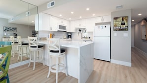 Une cuisine moderne avec des meubles blancs, un îlot central et un coin repas avec des chaises blanches.