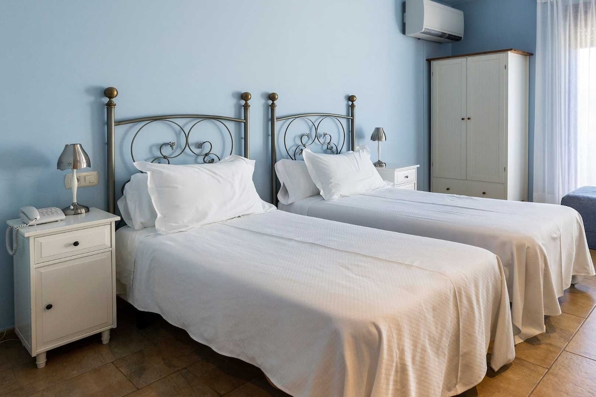 A hotel room with two beds, a wardrobe, a bedside lamp, and a telephone on the nightstand.