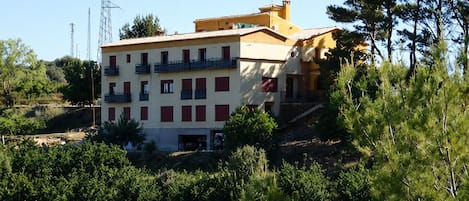 A multi-story building with balconies, surrounded by greenery and trees.