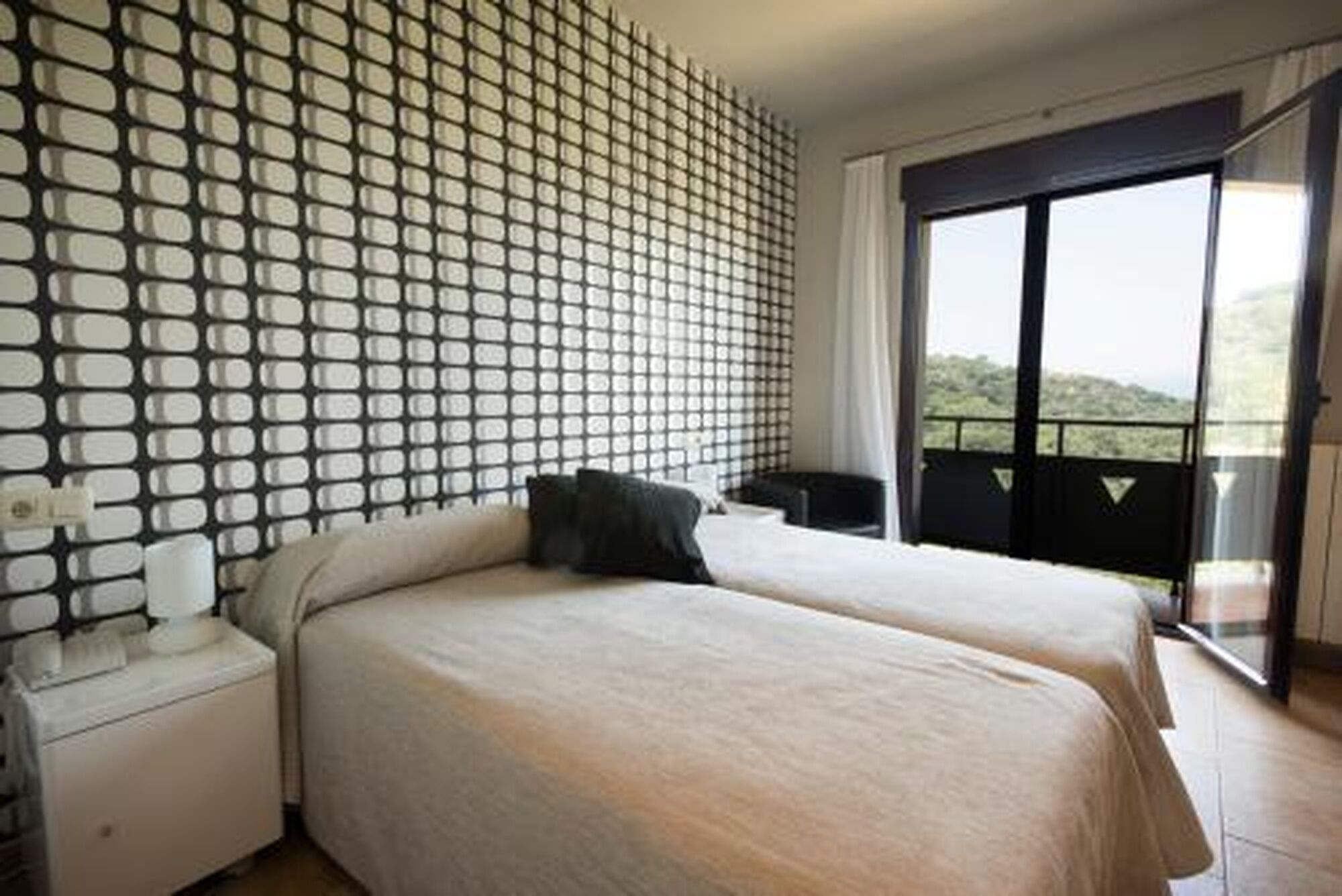 Een hotelkamer met een bed, een nachtkastje, een raam met uitzicht en een behang met patroon.