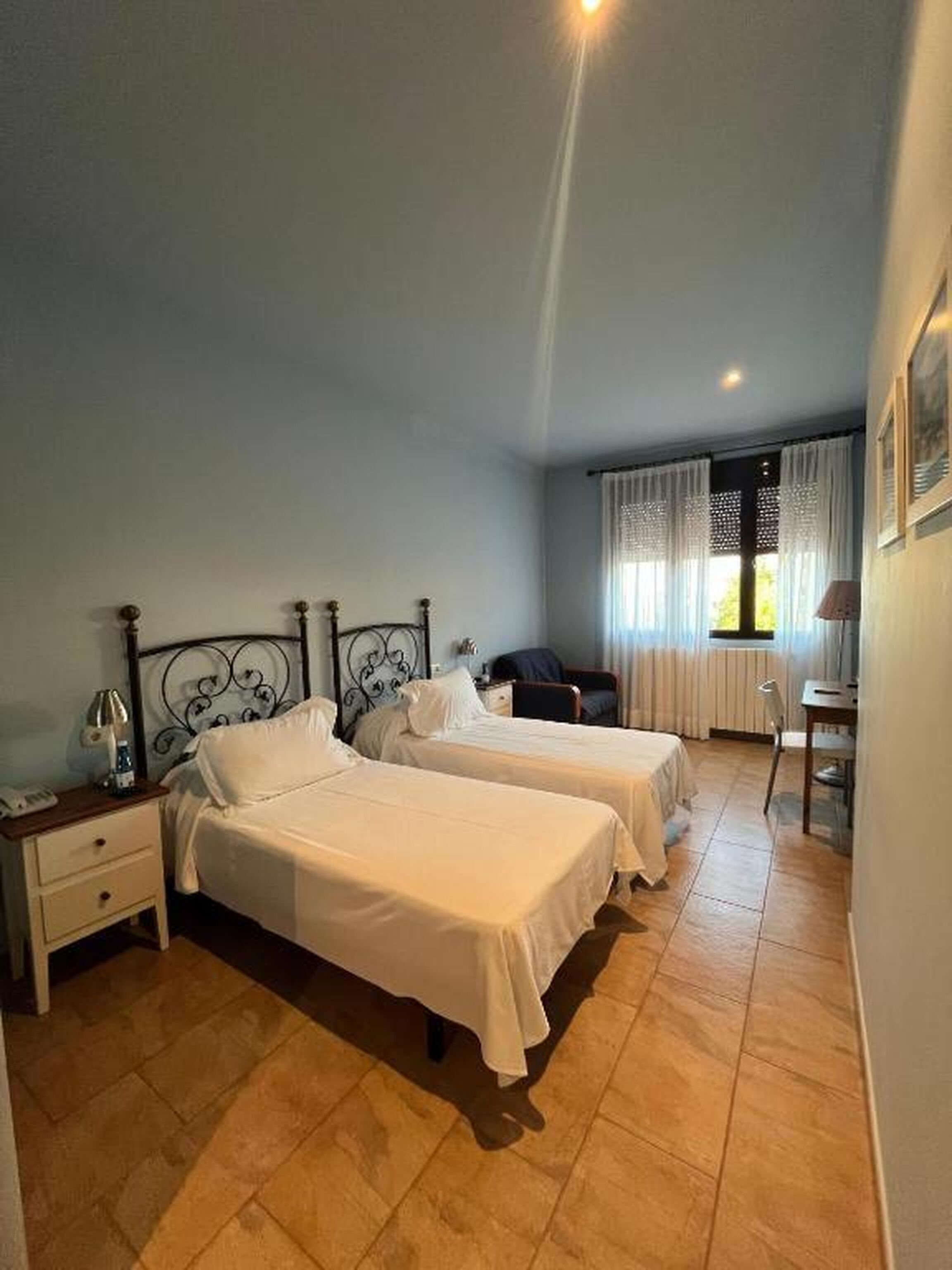 Een hotelkamer met twee bedden, een bureau, een stoel en een raam met gordijnen.